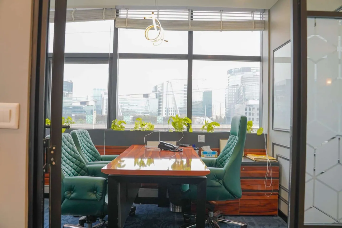 Director cabin behind a glass door, teal leather chairs and a desk facing a city skyline window — AIHP managed office, Gurgaon
