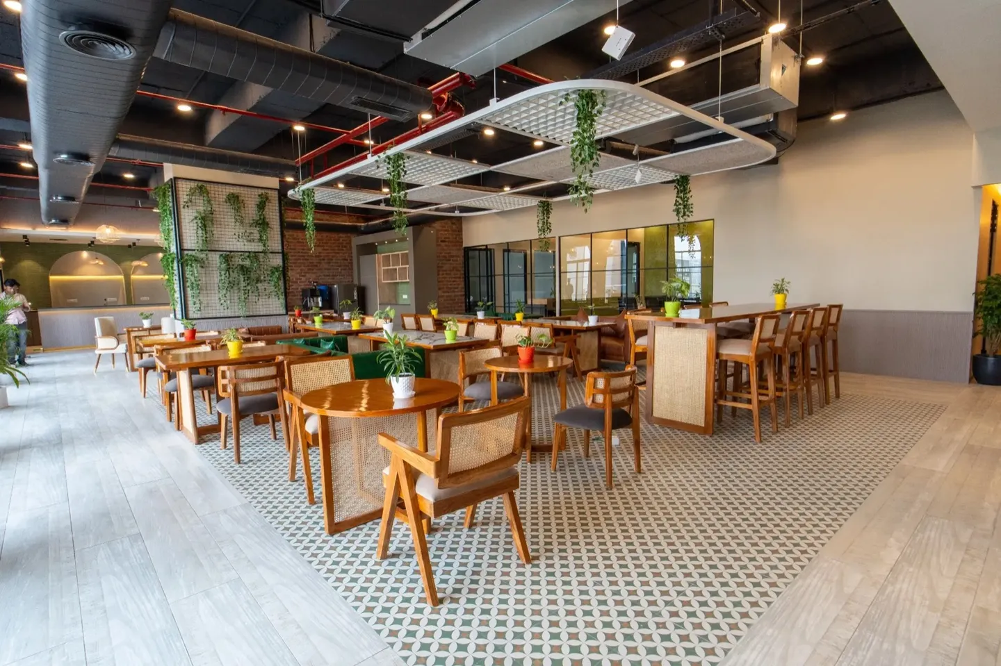 Open pantry-cafe with round and high tables, cane chairs, hanging planters and patterned tile flooring — AIHP managed office, Gurgaon