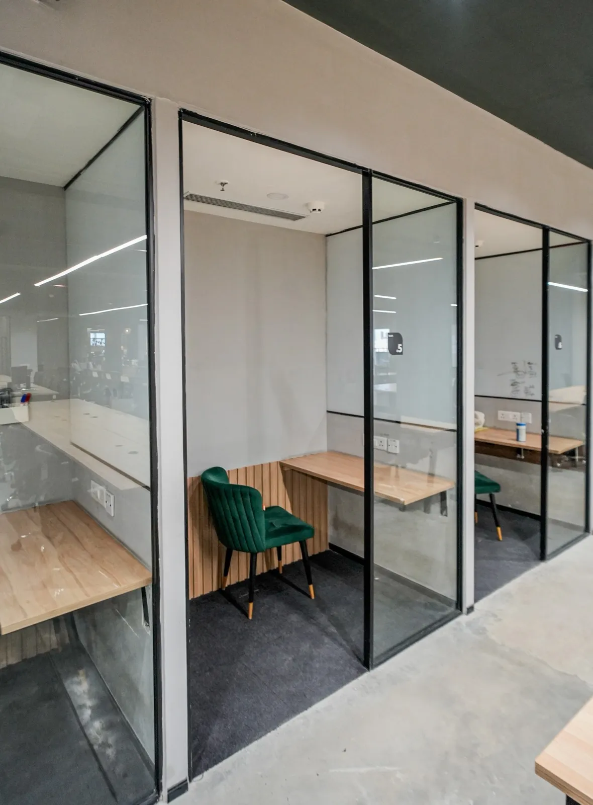 Glass-walled focus pod with a wooden ledge desk and green velvet armchair — AIHP managed office, Gurgaon