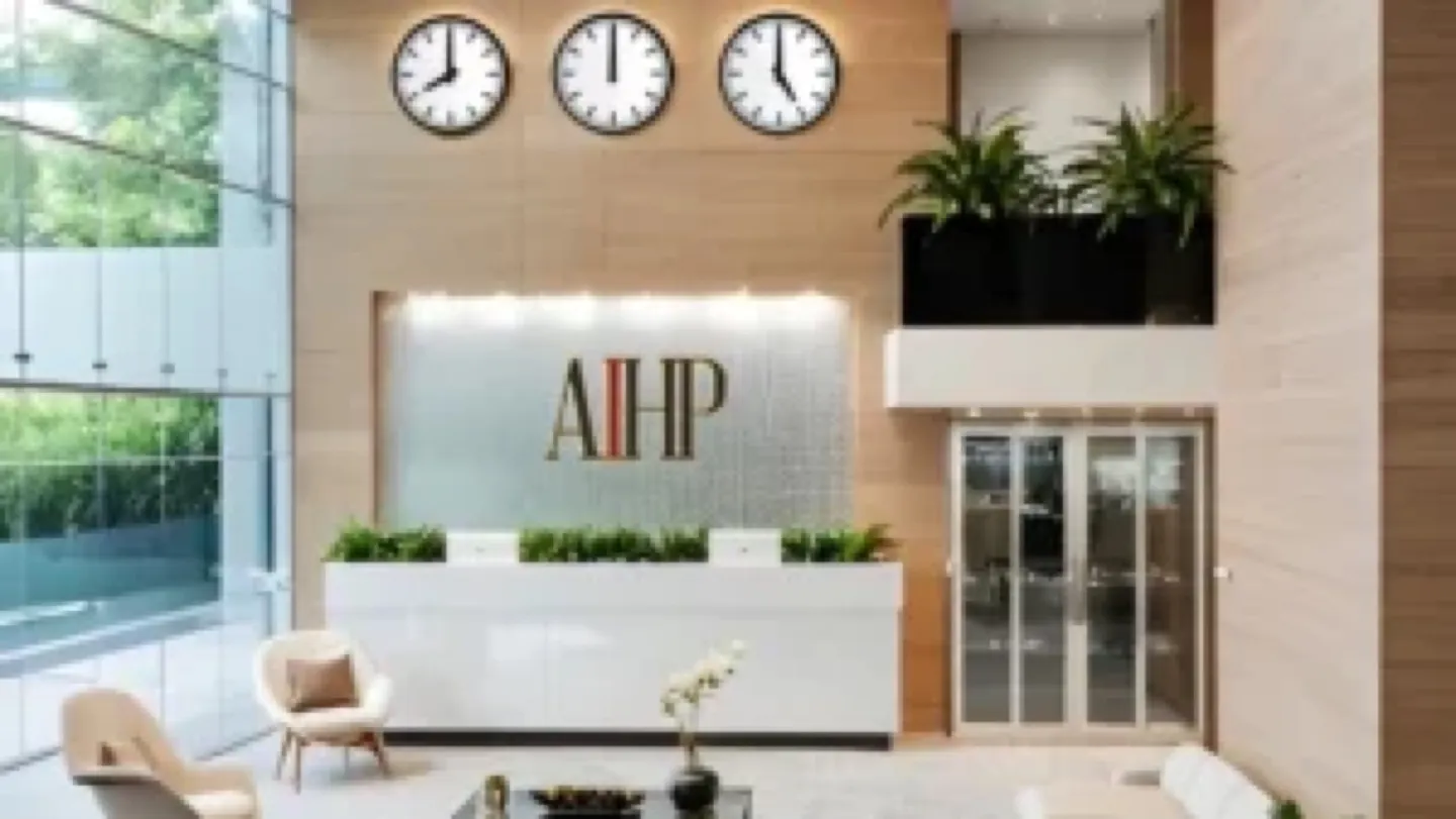 Bright lobby with three world clocks above an AIHP logo wall and white desk — AIHP managed office, Gurgaon